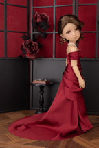 Doll in a red gown standing in a room with a decorative wall and table.