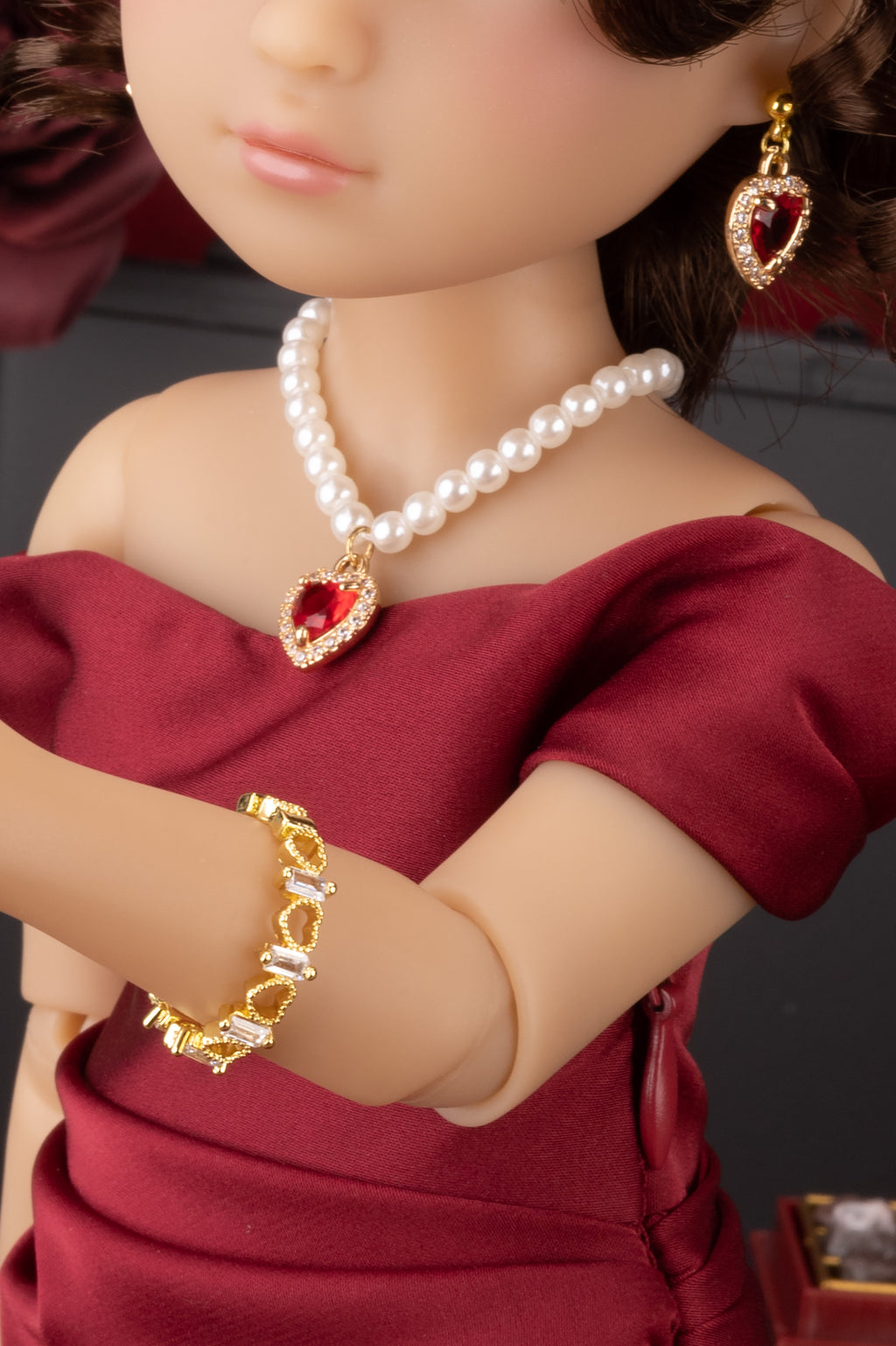 Doll wearing a red dress with gold jewelry including earrings and a bracelet.