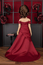 Doll in a red dress standing in front of a decorative wall with roses.