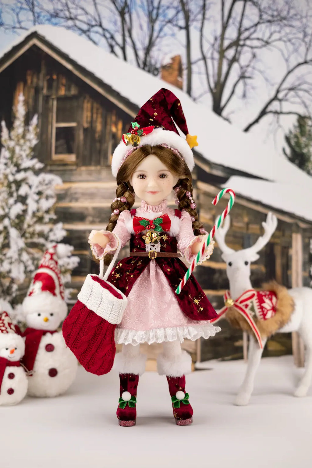 Christmas-themed doll with a snowy background featuring a house, reindeer, and snowman.