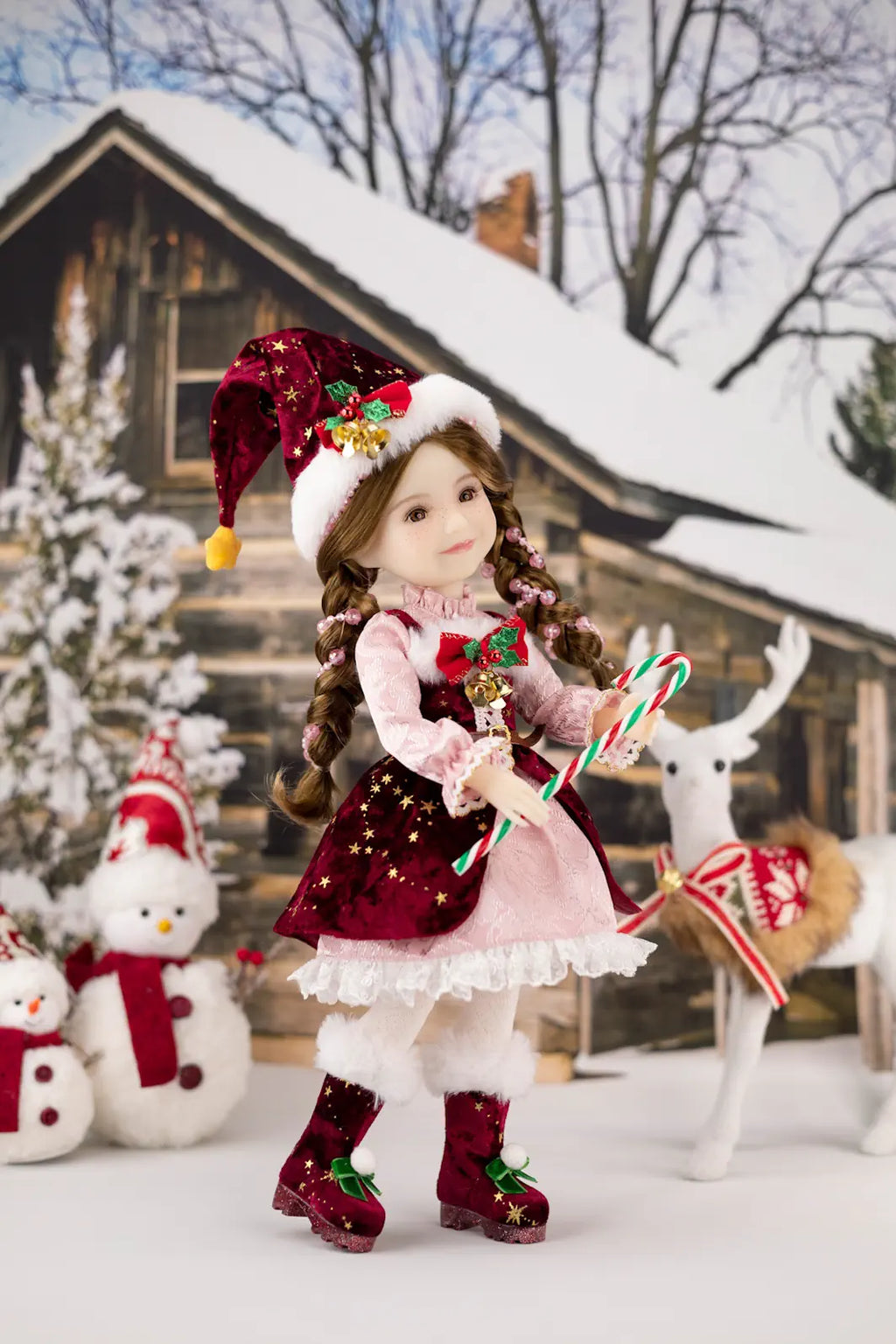 Christmas-themed doll in a snowy scene with a house, reindeer, and snowman.
