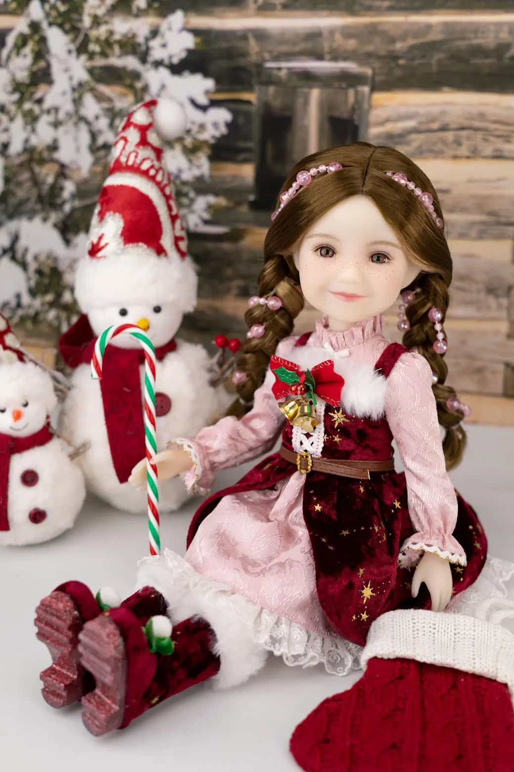 Doll in a festive setting with snowmen and a Christmas tree.