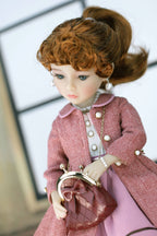 Doll wearing a pink coat and holding a matching handbag with a blurred background