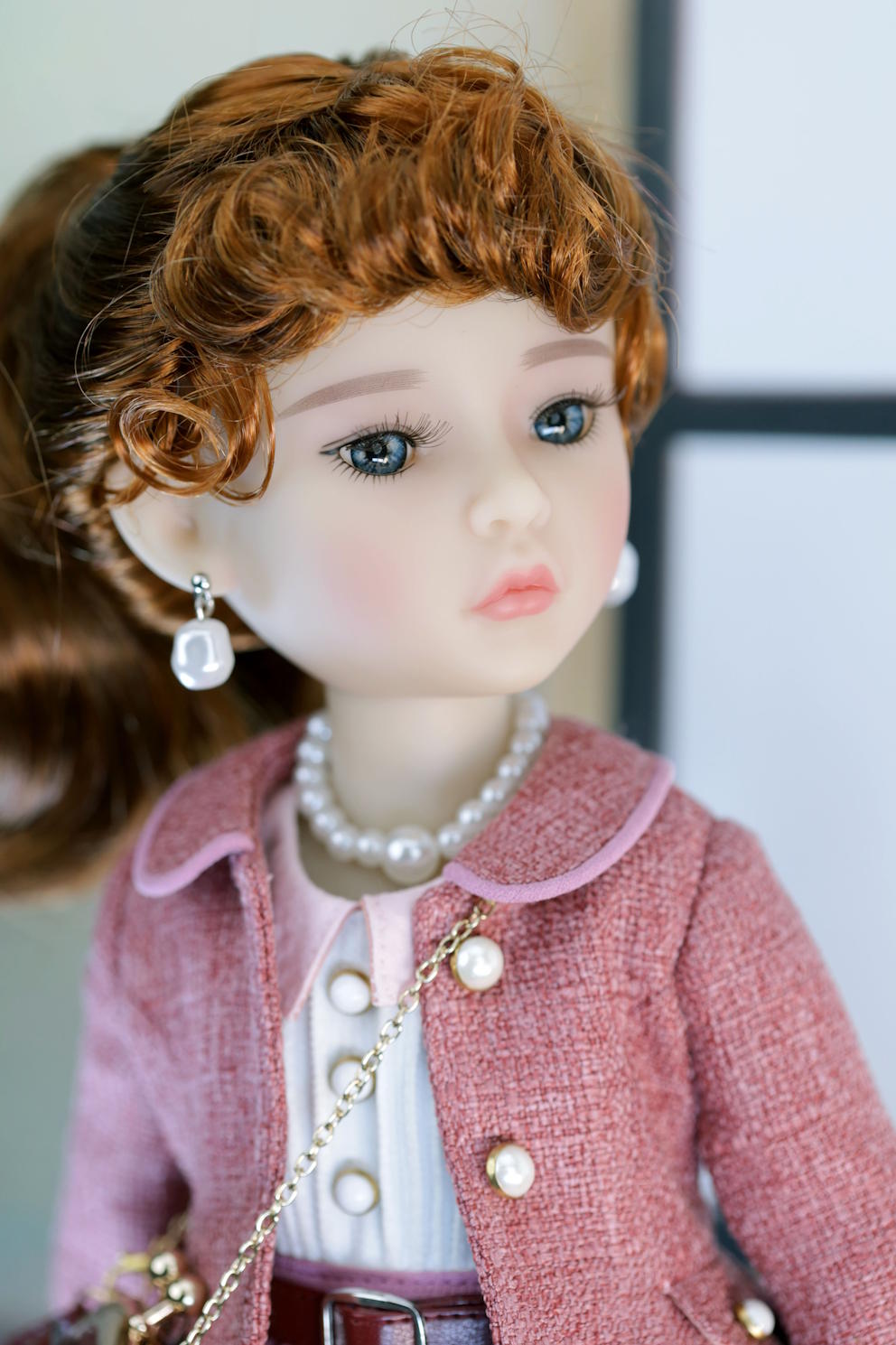 Detailed doll with red hair, wearing a pink coat and pearl accessories.