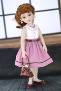 Doll in a pink dress holding a red handbag against a blurred indoor background