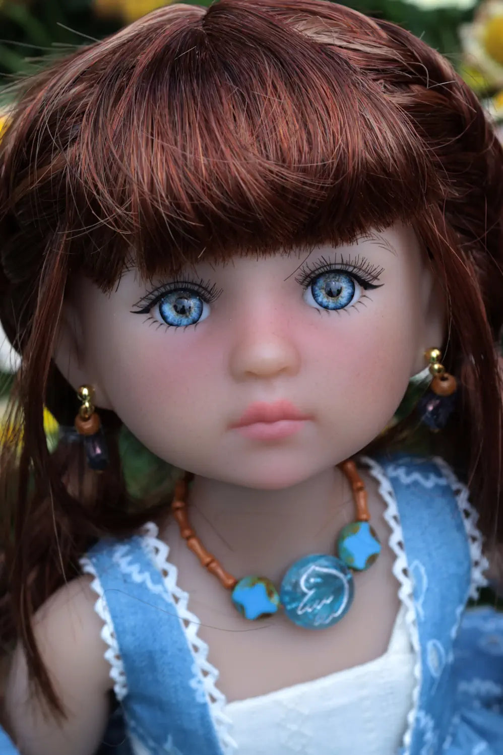 Close-up of a doll with brown hair, blue eyes, and wearing a blue dress with a necklace.