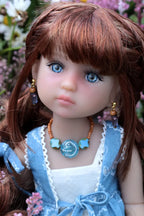 Close-up of a doll with brown hair and blue eyes, wearing a blue dress and necklace.