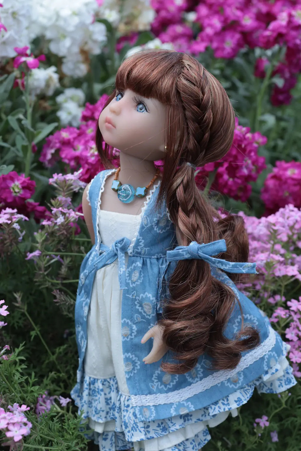 Doll with long brown hair and a blue dress standing among pink flowers