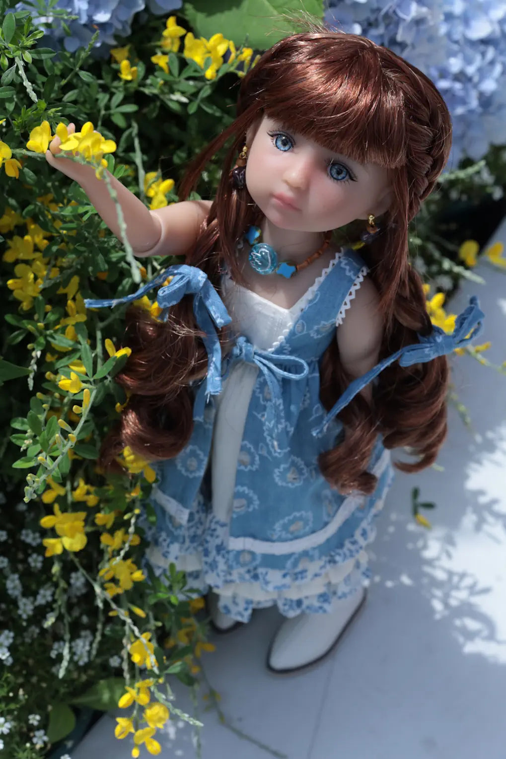 Doll with long brown hair and blue dress standing among yellow flowers