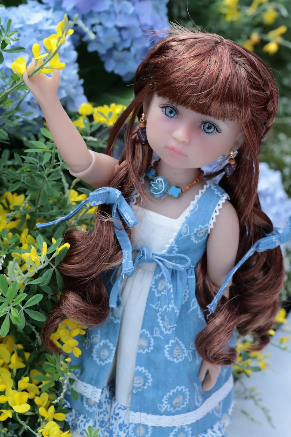 Doll with long brown hair and blue eyes, wearing a blue dress, surrounded by flowers.
