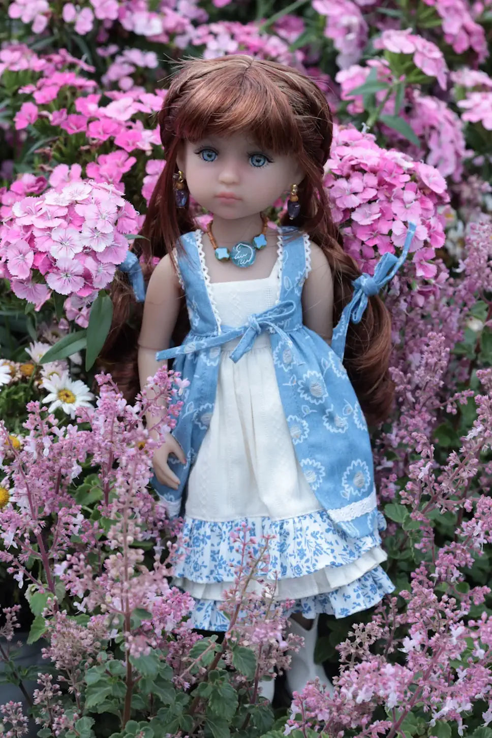 Doll in a blue and white dress standing among pink flowers