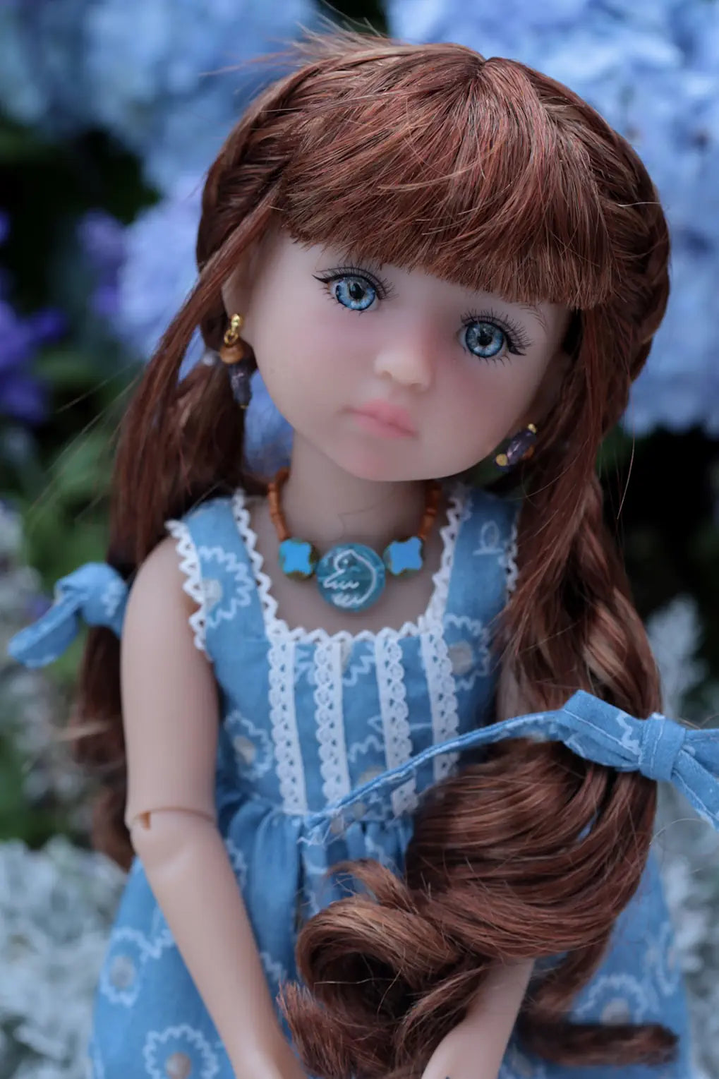 Doll with long brown hair and blue dress against a blurred natural background