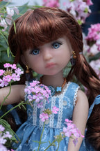 Doll with brown hair and blue eyes, wearing a blue dress, surrounded by pink flowers.