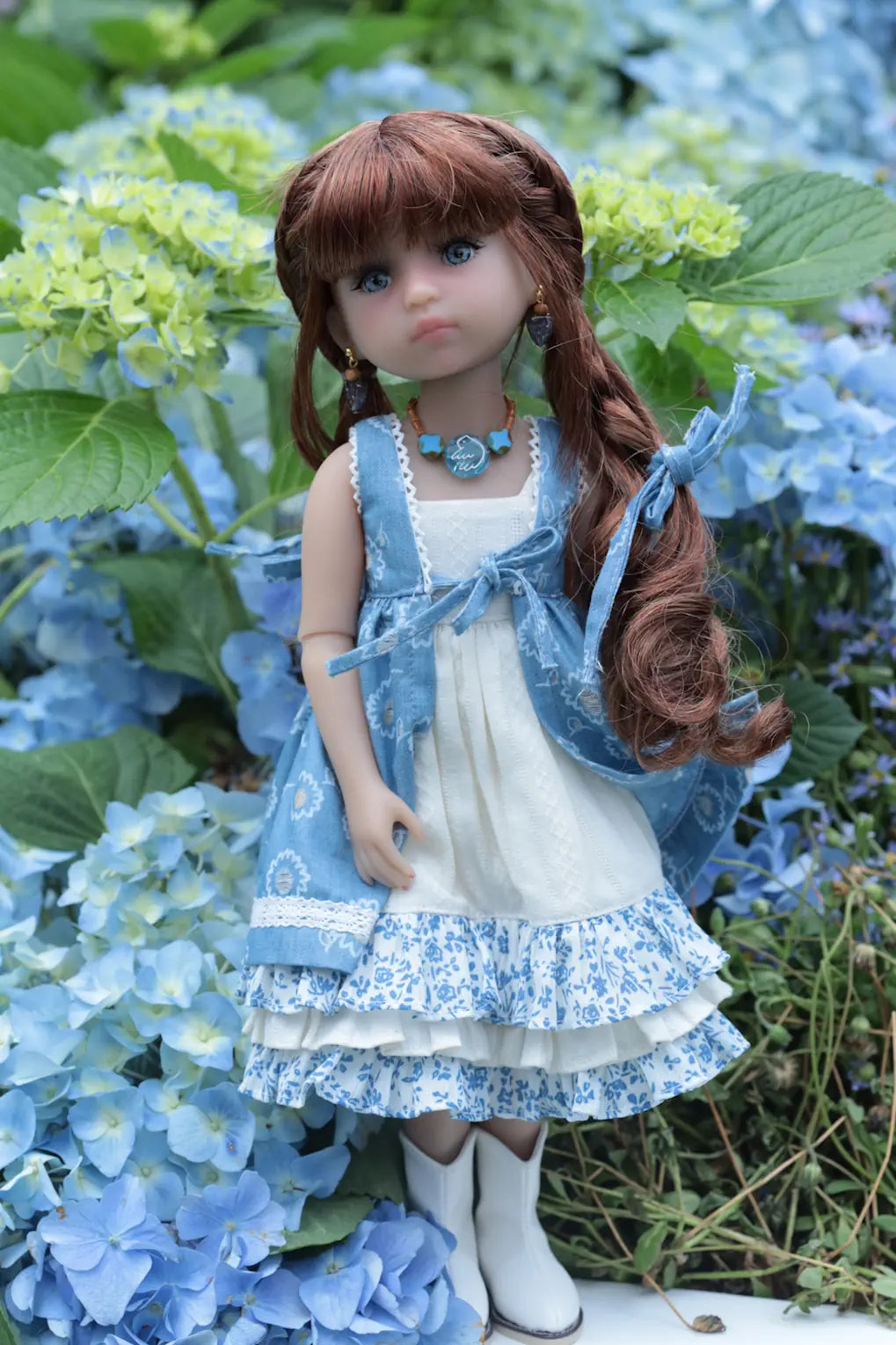 Doll in a blue and white dress standing among hydrangeas