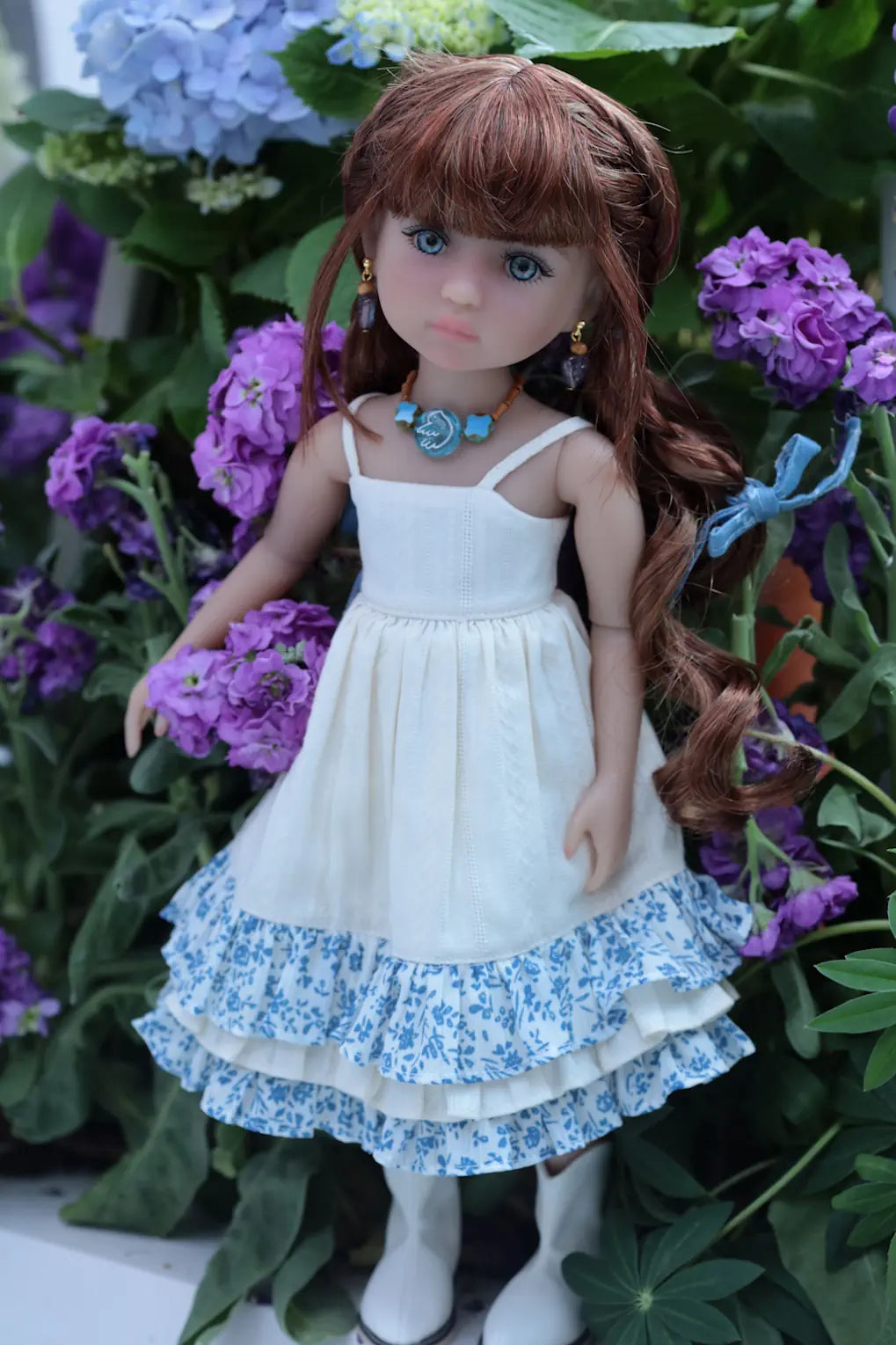 Doll in a white dress with blue floral patterns standing among flowers