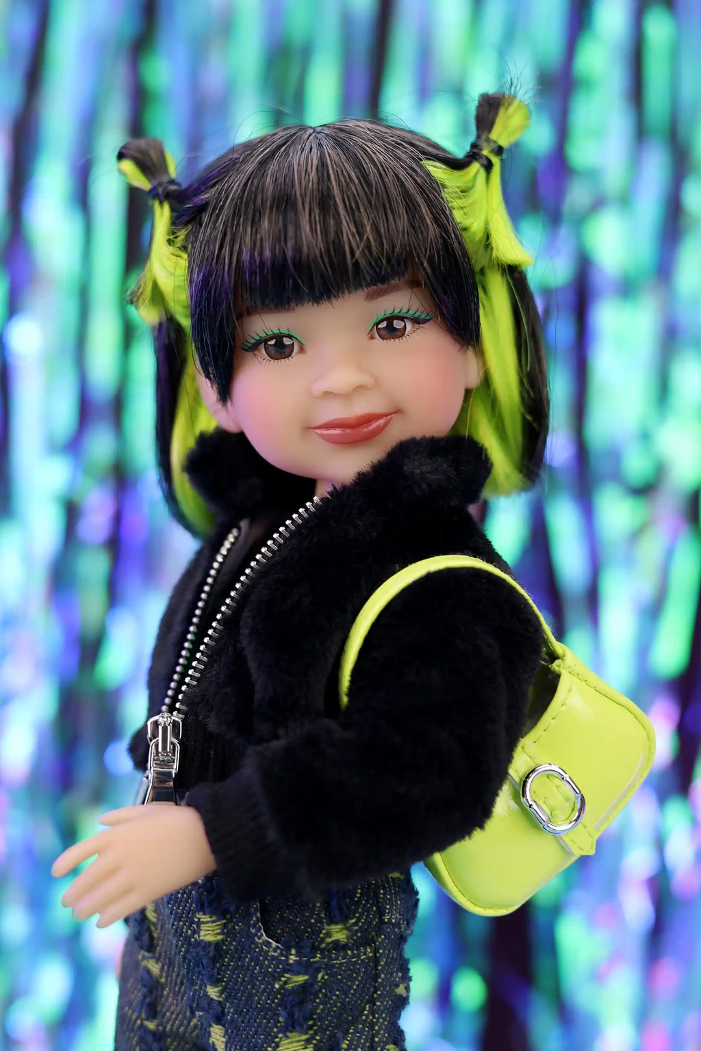 Doll with black hair styled in pigtails, wearing a black jacket and colorful outfit against a blurred multicolored background.