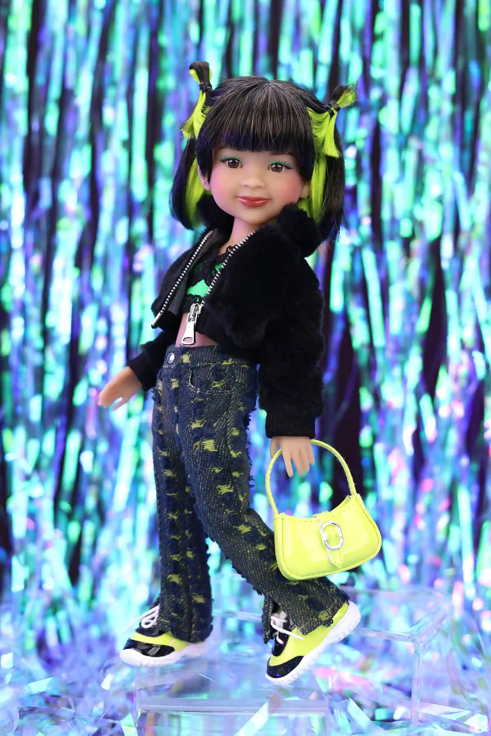 Doll with black jacket, patterned pants, and yellow shoes holding a yellow handbag against a colorful, abstract background.