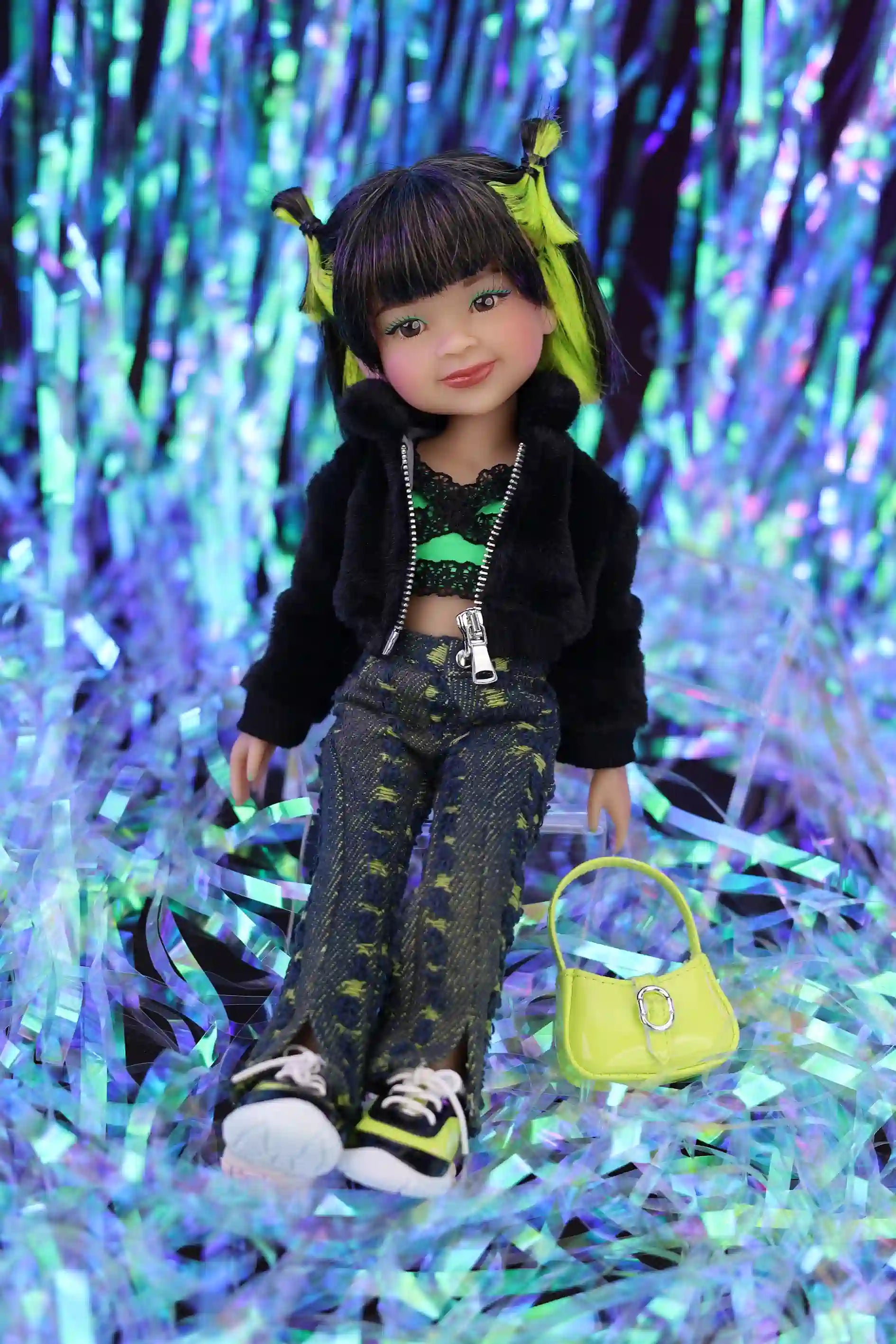 Doll with black jacket and green pants sitting on a glittery purple and blue background