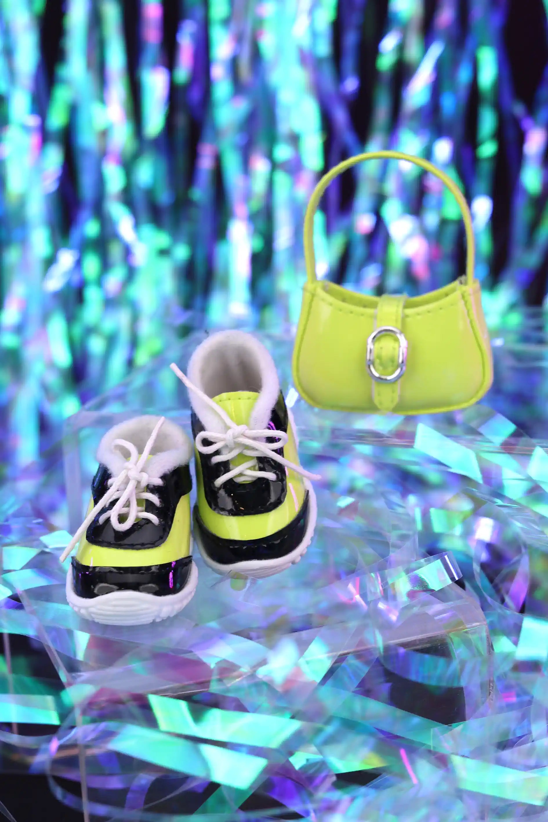 Pair of black and white sneakers with yellow accents and a green handbag on a reflective surface with colorful tinsel background.