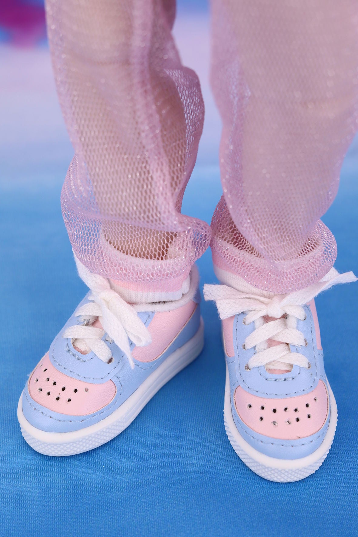 Doll's pastel blue and pink shoes with white laces on a blue background