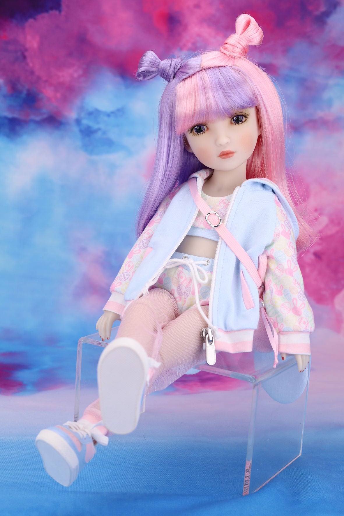 Doll with pastel-colored hair and outfit sitting on a clear chair against a colorful background