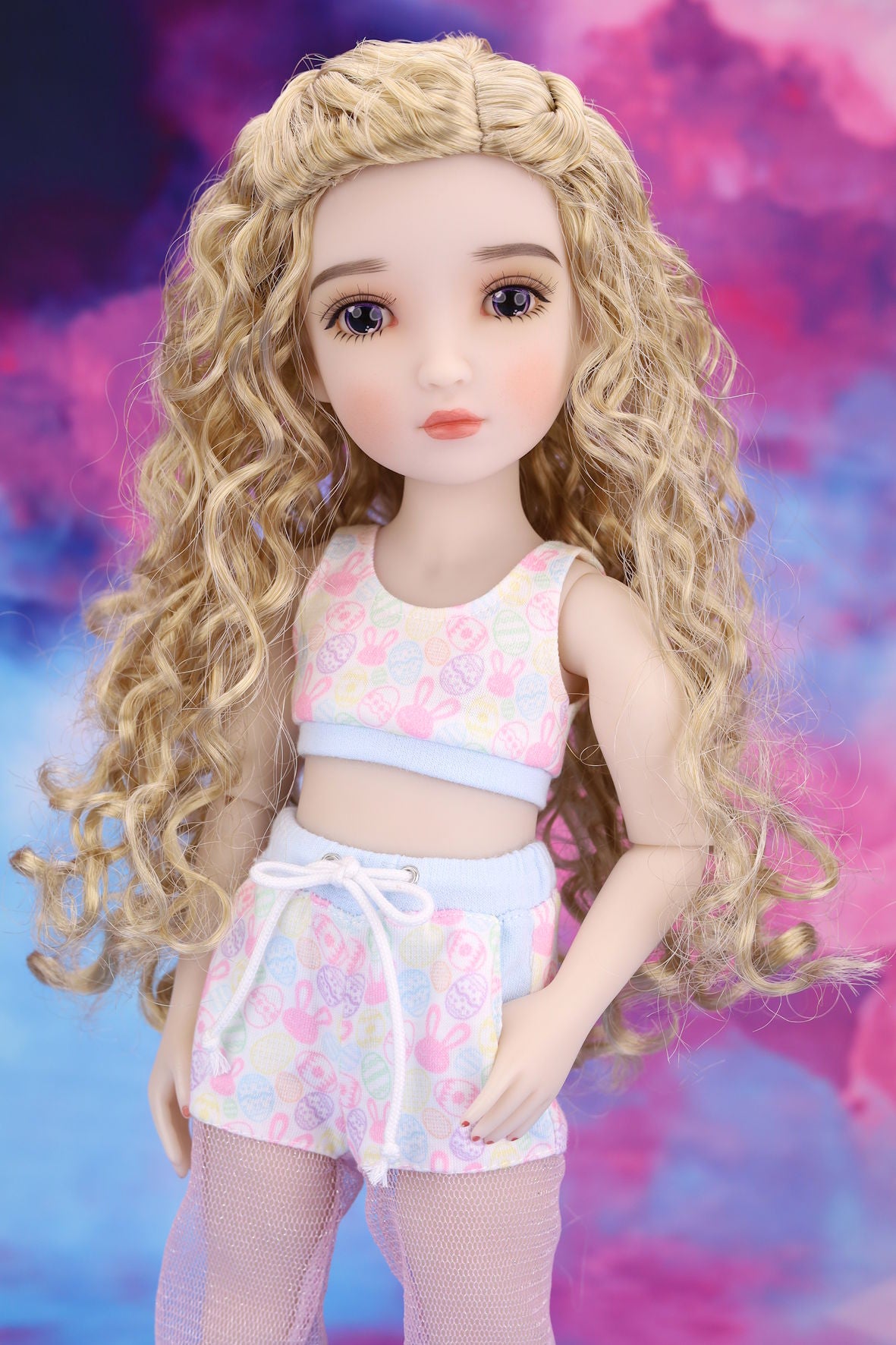 Doll with long blonde hair wearing a colorful outfit against a multicolored background