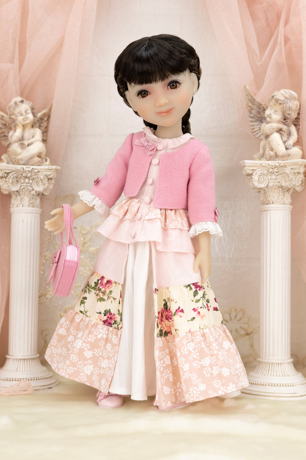 Doll in a pink outfit with floral skirt standing in front of decorative columns and cherubs.