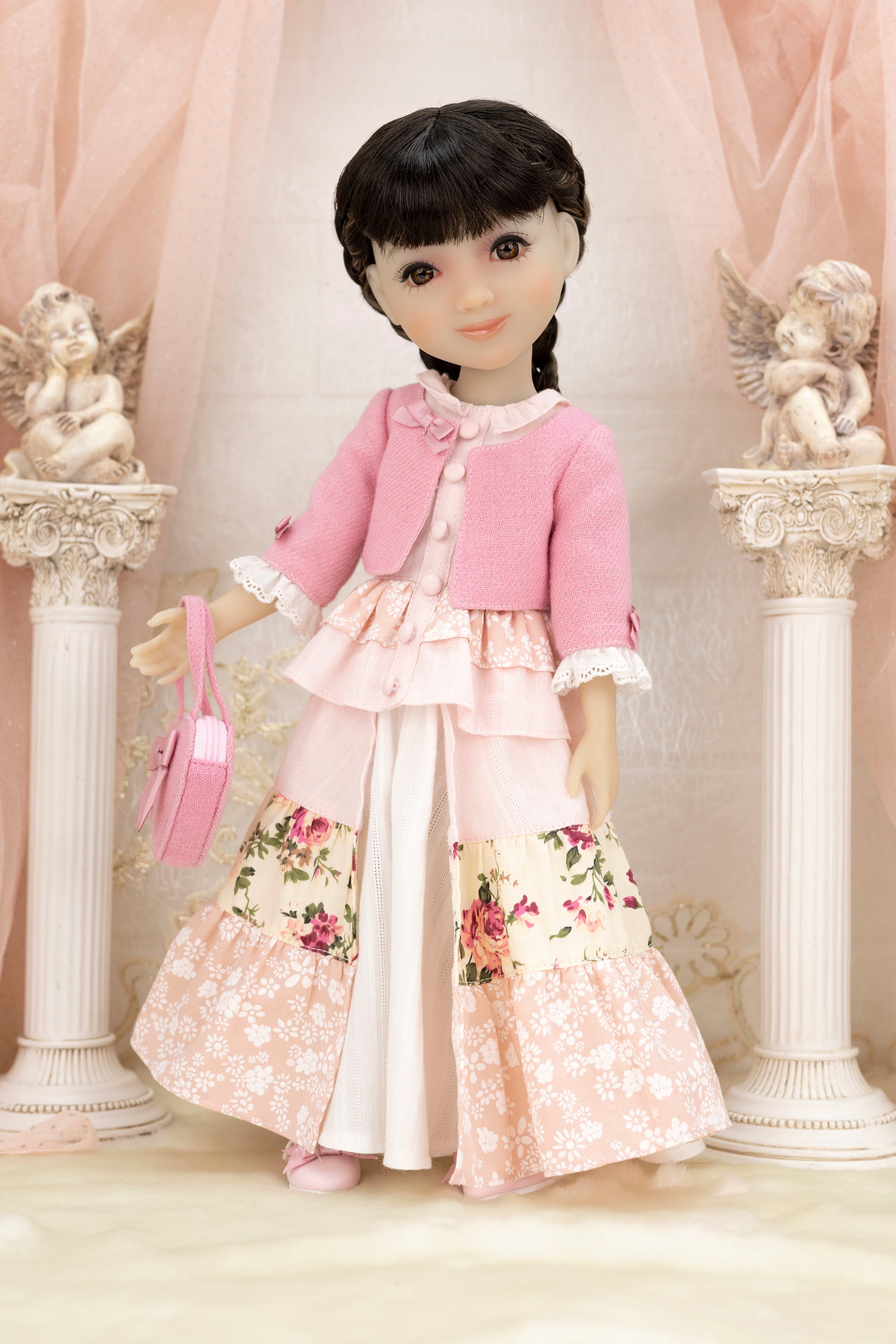 Doll in a pink outfit with floral skirt standing in front of decorative columns and cherubs.