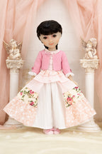 Doll wearing a pink cardigan and floral dress with cherub statues in the background