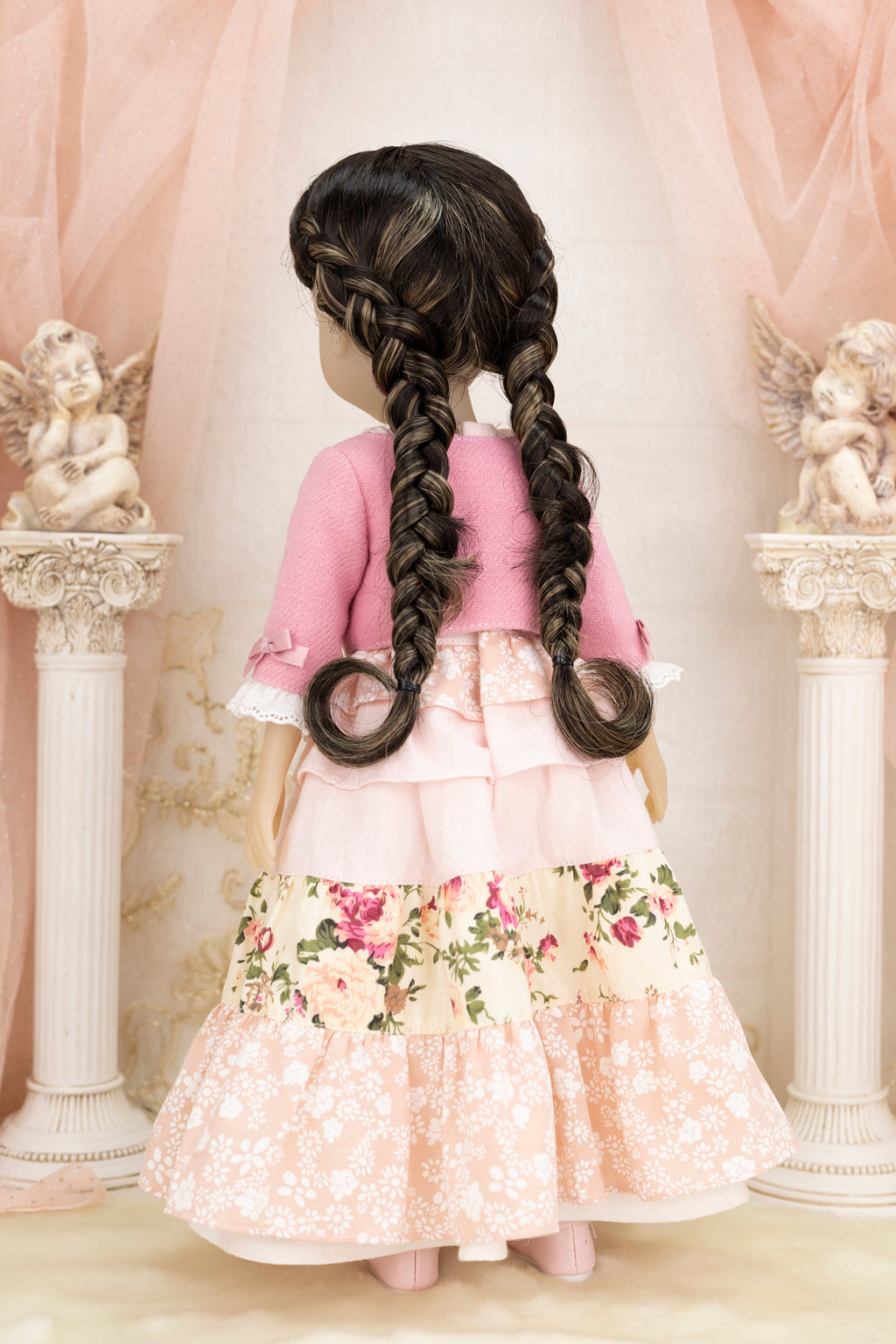 Doll with long braided hair wearing a pink dress in an elegant setting.