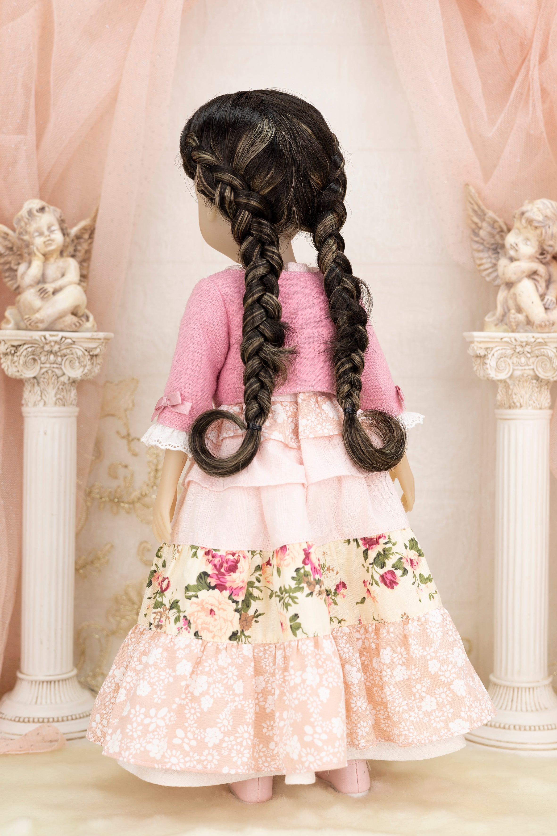 Doll with long braided hair wearing a pink dress in an elegant setting.