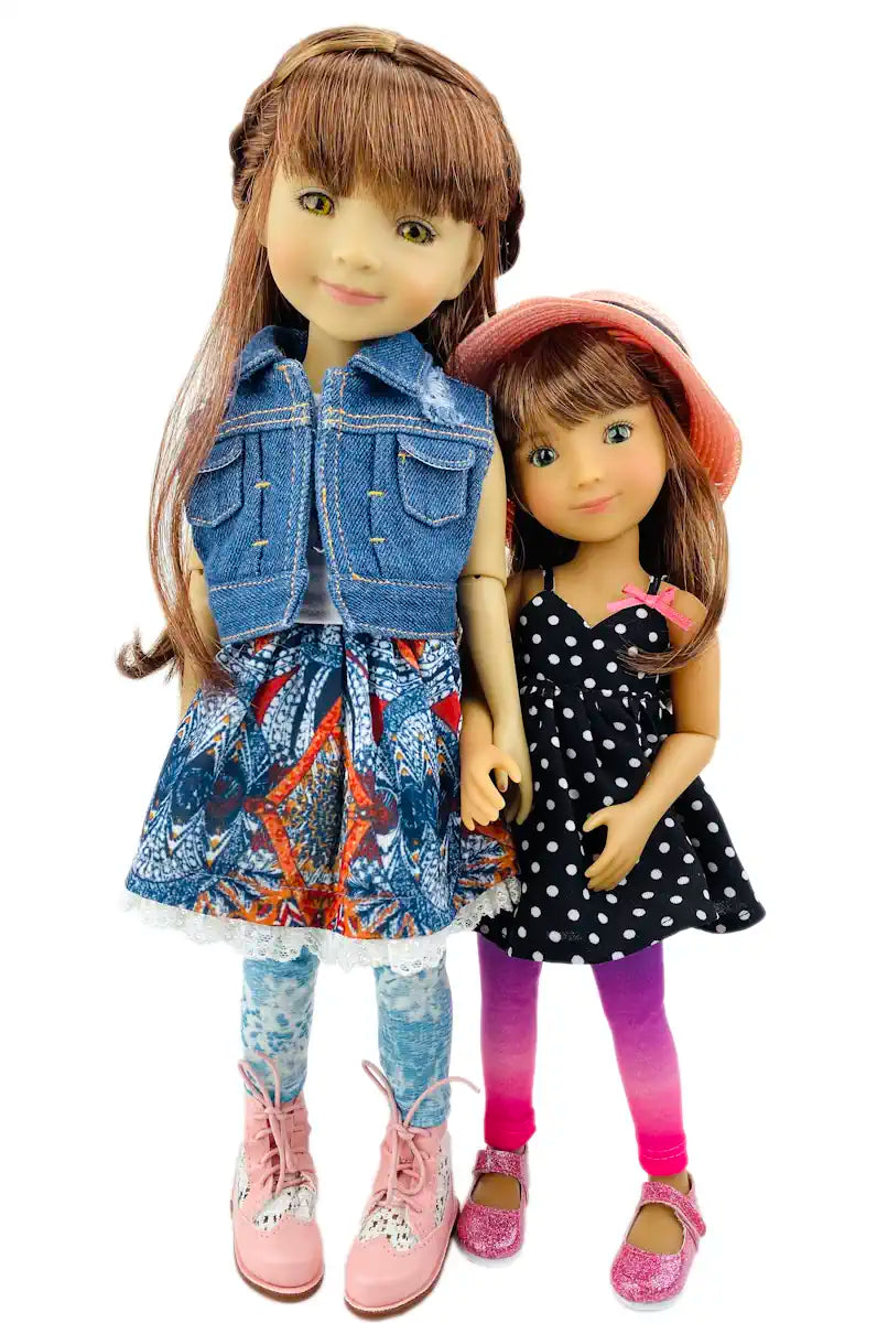 Bella and Bailey with one wearing a denim vest and colorful dress, the other in a polka dot dress and pink hat, on a white background.