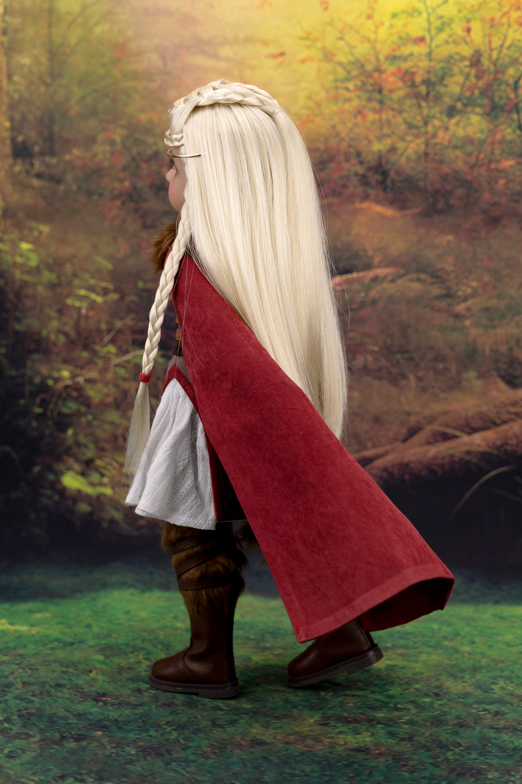 Person in a red cloak and blonde hair standing in a forest setting