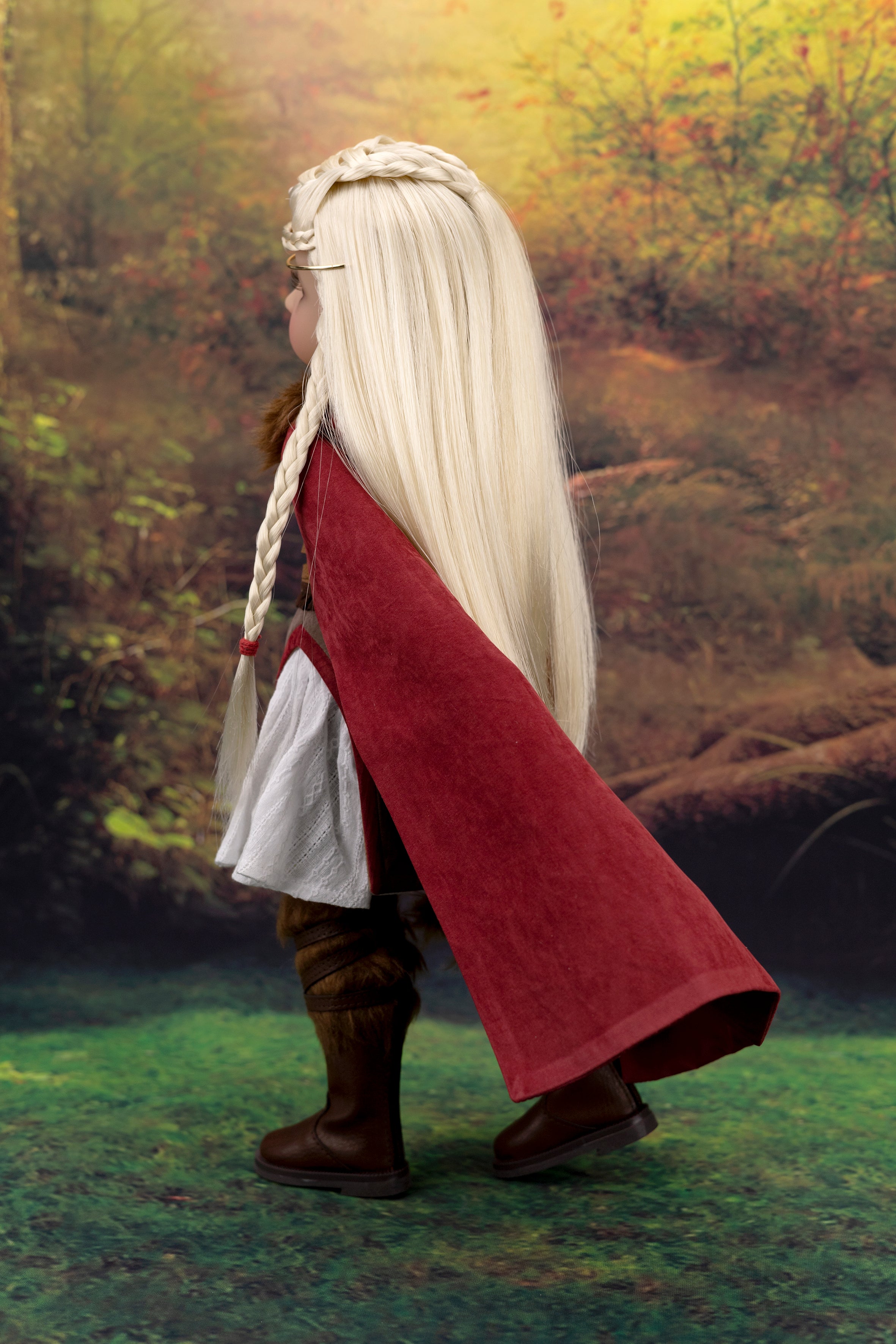 Person in a red cloak and blonde hair standing in a forest setting