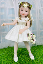 Doll in a white dress with a floral headband and bouquet on a grassy surface.