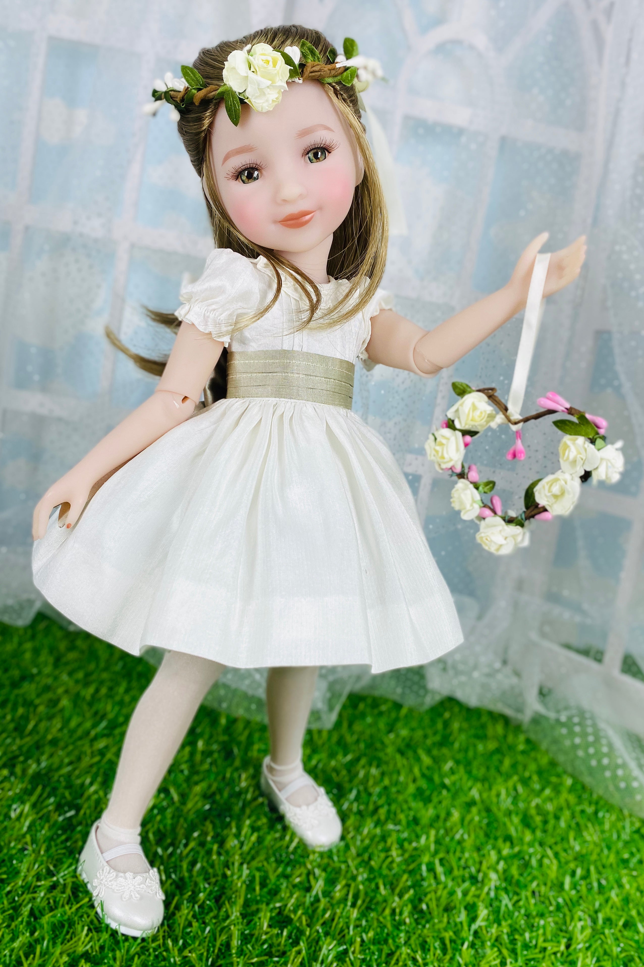 Doll in a white dress with floral accessories on a grassy surface