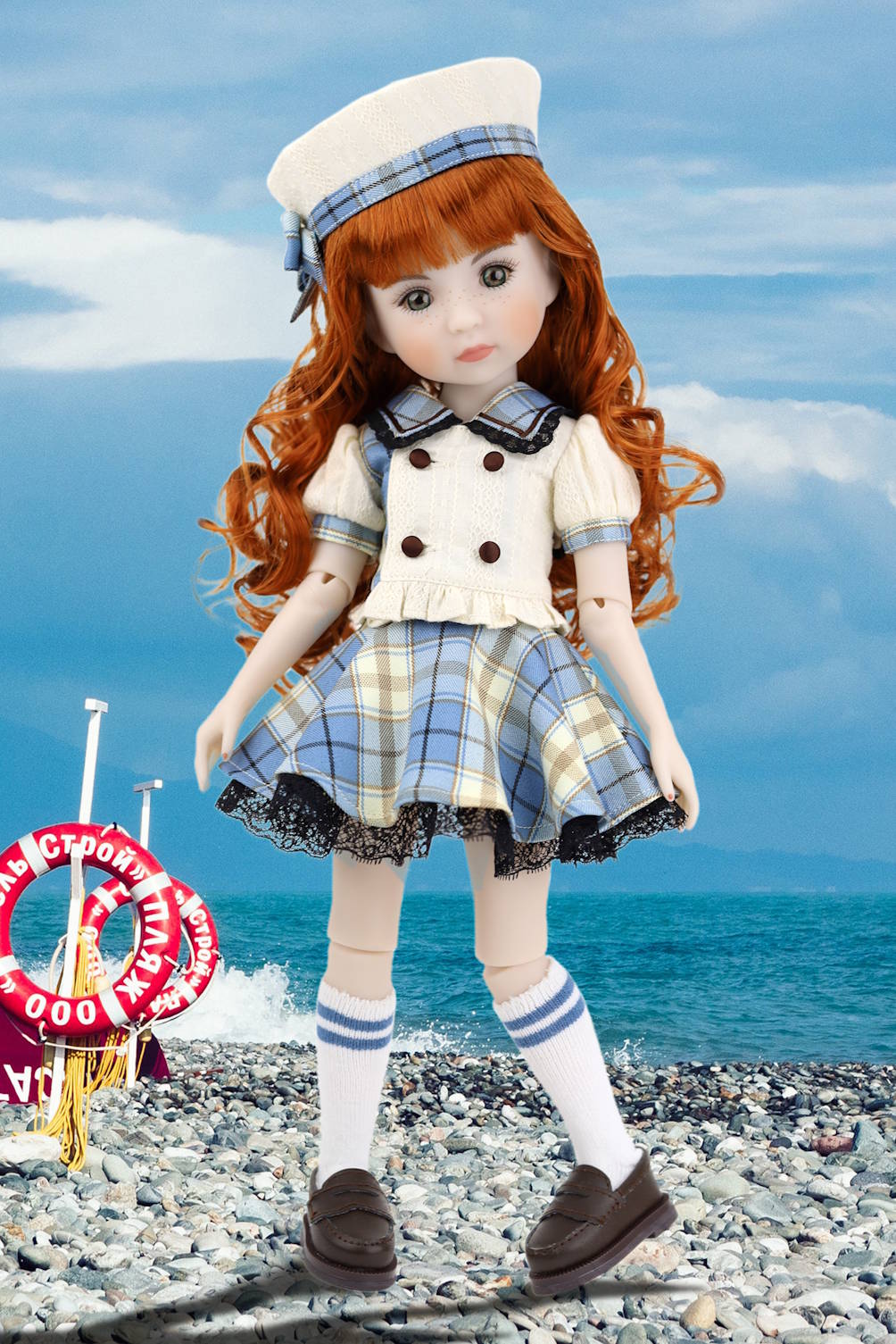 Doll in a nautical outfit standing on a pebbly beach with a blue sky.