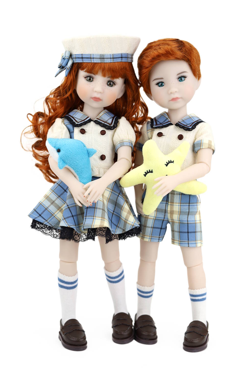 Two dolls with red hair, wearing school uniforms, holding stuffed animals on a white background.