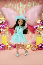 Doll in a turquoise dress and hat with colorful balloons and decorations in the background