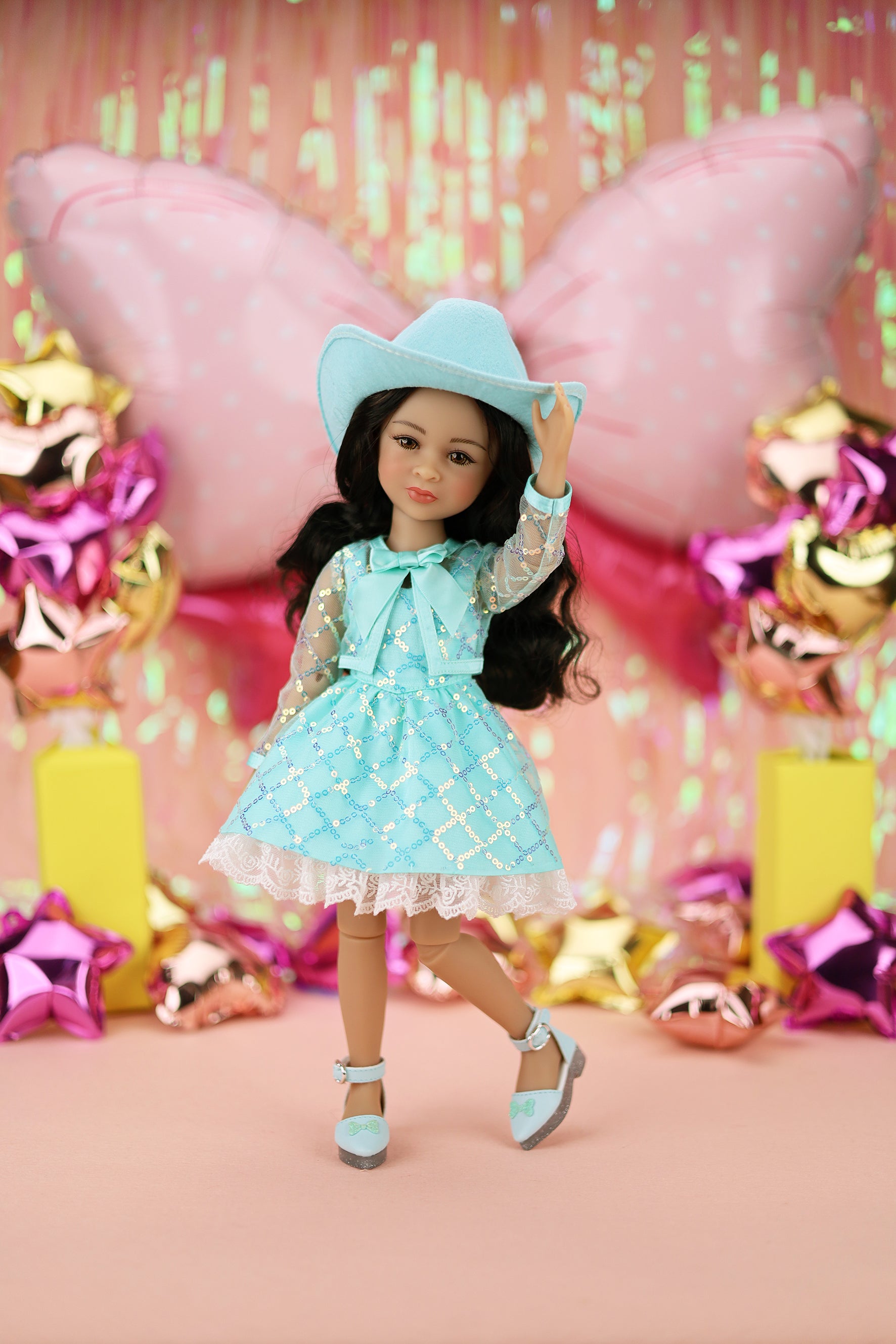 Doll in a turquoise dress and hat with colorful balloons and decorations in the background
