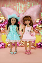 Two dolls in dresses and hats standing together with a festive background.