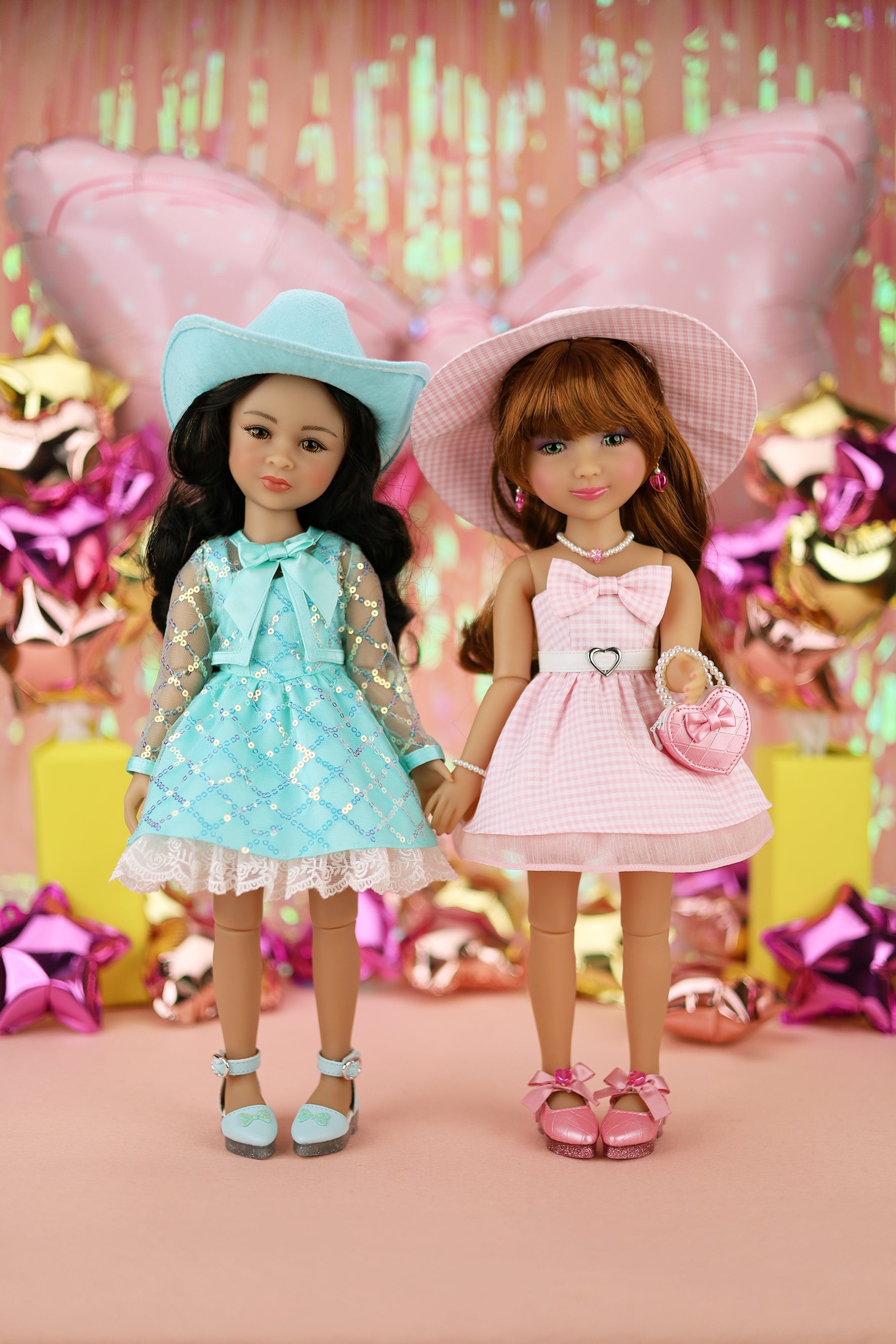 Two dolls in dresses and hats standing together with a festive background.