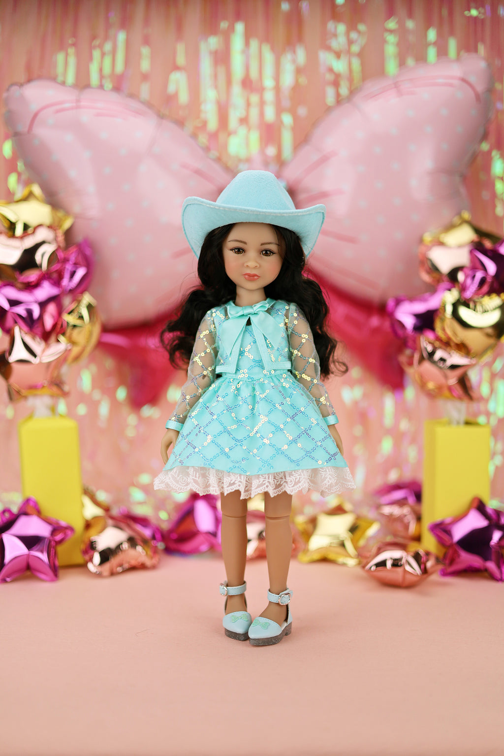 Doll in a turquoise outfit with cowboy hat against a festive background with balloons and decorations.