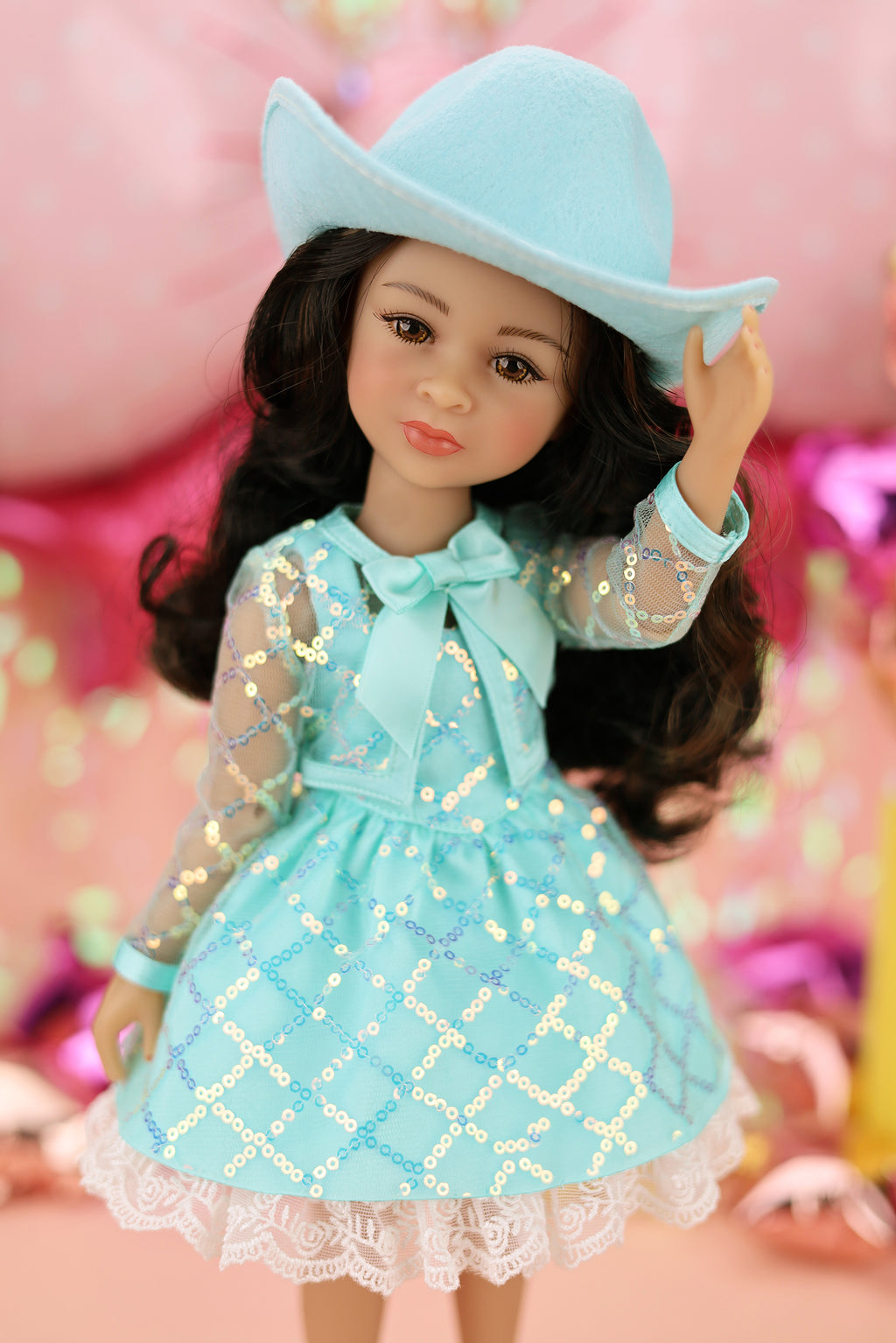 Doll wearing a turquoise dress and hat against a pink background