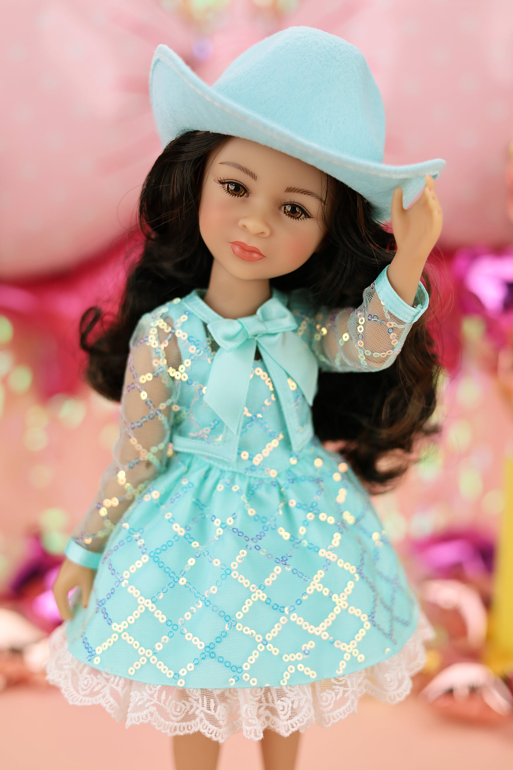 Doll wearing a turquoise dress and hat against a pink background