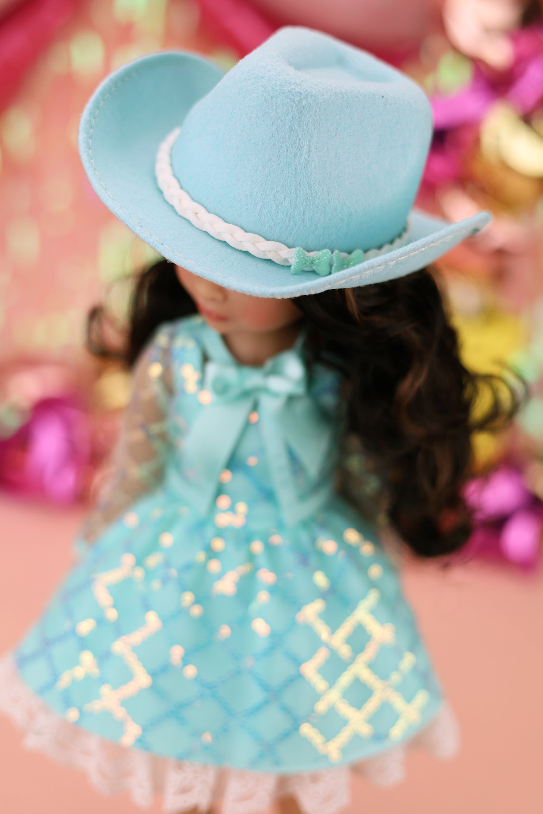 Doll wearing a blue dress with a pattern and a matching hat against a colorful background
