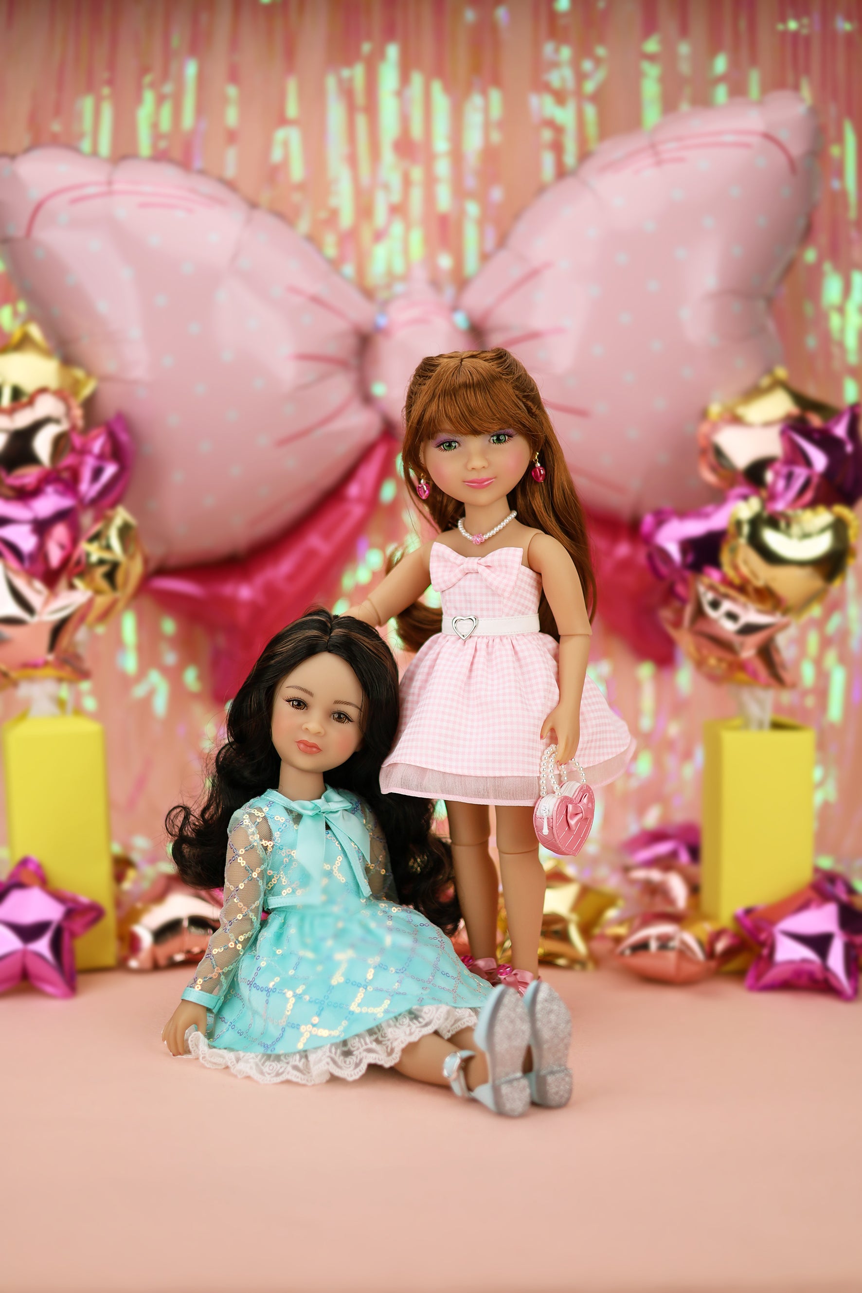 Two dolls in dresses with colorful balloons and decorations in the background