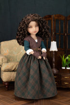 A doll with long curly brown hair wearing a detailed historical-style dress, posed in a miniature room setting with a chair, cabinet, and lamp.