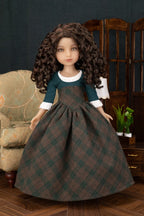 A doll with long curly brown hair wearing a dark green and brown plaid dress with white collar and cuffs, posed in a styled room setting with a chair, wooden screen, and small plant.