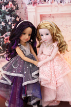 Two dolls in formal dresses standing next to each other with a decorated Christmas tree in the background.